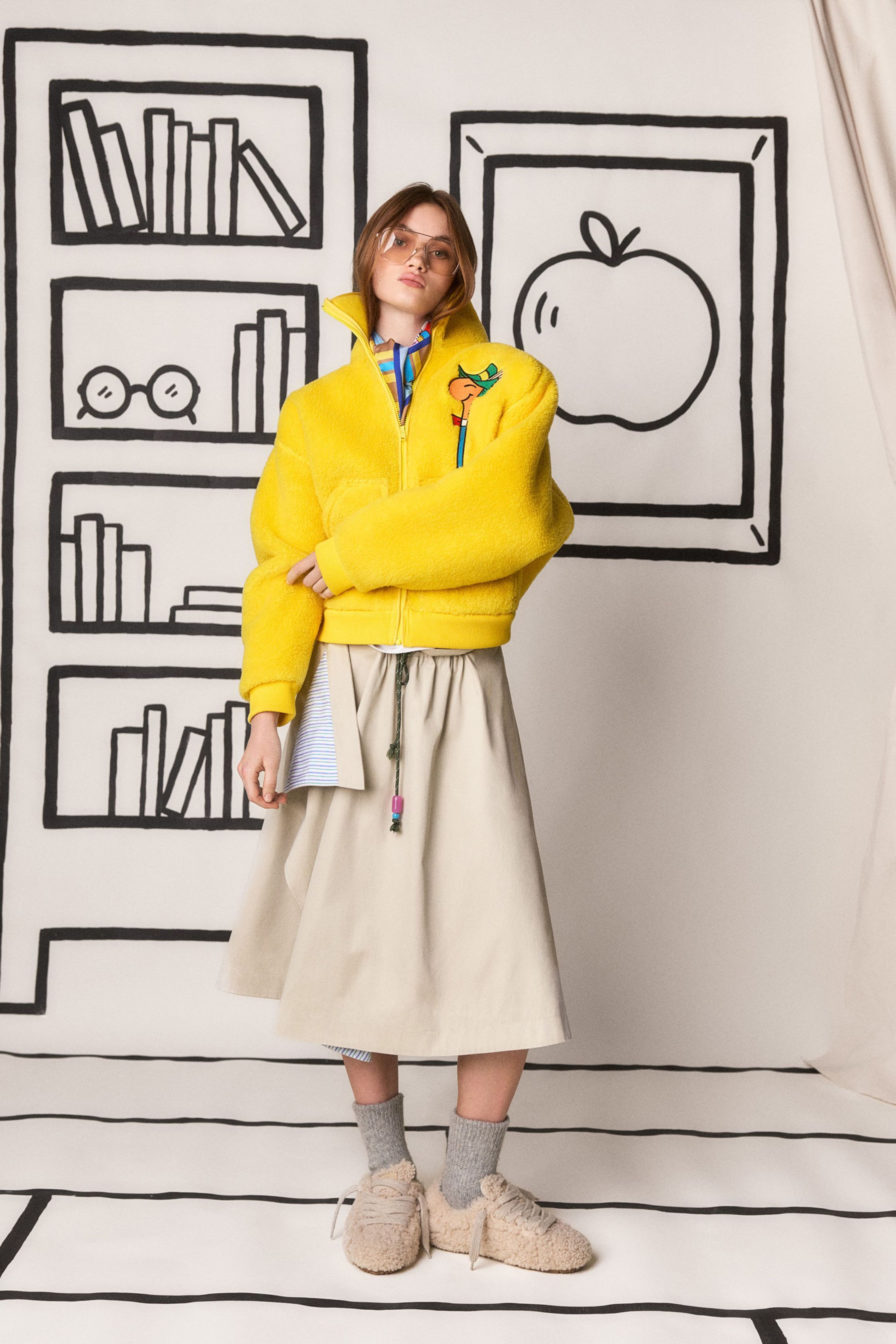 Mira Mikati 本季继续以充满童趣的视觉语言构建一个轻松而充满想象力的衣橱：卡通刺绣、学院领带、彩色针织和宽松半裙构成一个介于校园与艺术工作室之间的世界。鲜亮黄色、菱格针织和手绘背景让整场秀像一本立体绘本，充满快乐与创意-顽石频道趋势研究